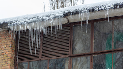 Icicles on the drainpipe and ditch. Incorrect installation of the drainage system, on which large icicles appear that pose a threat to the health and lives of people passing by.