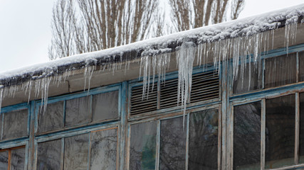 Icicles on the drainpipe and ditch. Incorrect installation of the drainage system, on which large icicles appear that pose a threat to the health and lives of people passing by.