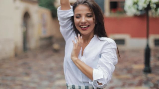 Happy young woman dancing and having fun with umbrella on the street of the old city. Beautiful firl looking and posing into the camera, small rain falling