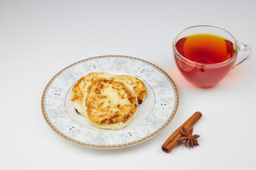 Cheesecakes on a saucer with jam and tea. cottage cheese pancakes or pancakes with strawberry jam and a Cup of tea on a white table. traditional Russian Breakfast. vertical view.
