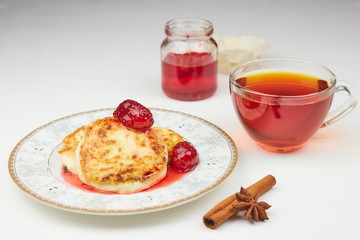 Cheesecakes on a saucer with jam and tea. cottage cheese pancakes or pancakes with strawberry jam and a Cup of tea on a white table. traditional Russian Breakfast. vertical view.