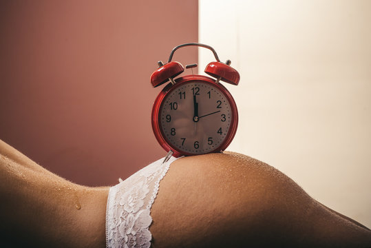 Wake up. Morning alarm clock on the naked female ass. Time and the dream. Aging. Skin and buttocks. Woman and time concept