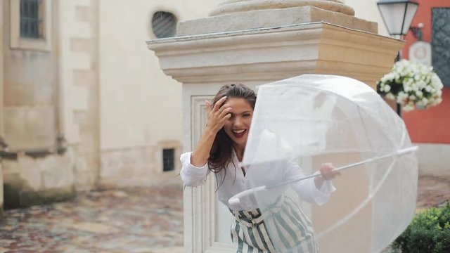 Happy young woman dancing and having fun with umbrella on the street of the old city. Beautiful firl looking and posing into the camera, small rain falling