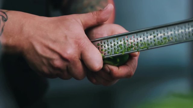 Hands man chef rubbing a lime peel on a grater in a restaurant kitchen cut fruit close up vegetarian organic preparation cooking food fresh citric slow motion