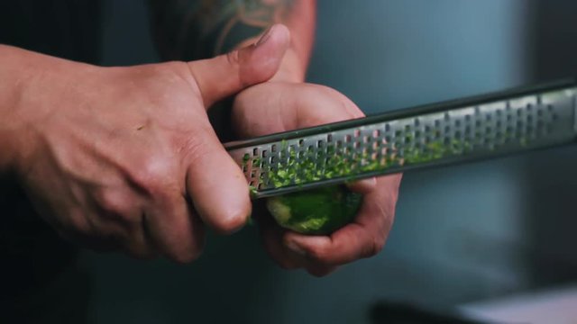 Close up hands man chef rubbing a lime peel on a grater in a restaurant kitchen cut fruit vegetarian organic meat preparation cooking food fresh citric slow motion