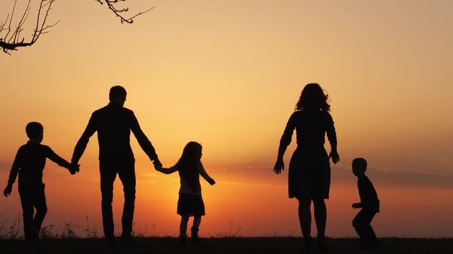 Silhouettes of happy family walking together in the meadow during sunset.