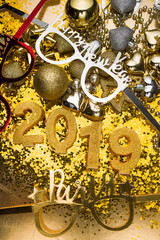 New Years Eve celebration background with champagn glass, 2019 number made with golden glitter candles, christmas decoration around, flatlay over a golden board, luxury  holiday concept