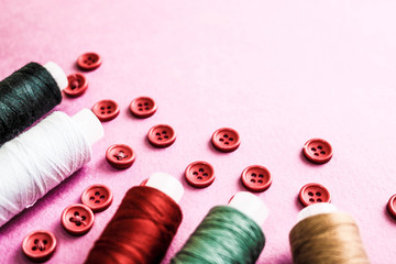 Beautiful texture with lots of round red buttons for sewing, needlework and skeins of spools of thread. Copy space. Flat lay. Pink, purple background