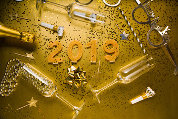 New Years Eve celebration background with champagn glass, 2019 number made with golden glitter candles, christmas decoration around, flatlay over a golden board, luxury  holiday concept