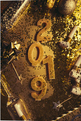 New Years Eve celebration background with champagn glass, 2019 number made with golden glitter candles, christmas decoration around, flatlay over a golden board, luxury  holiday concept