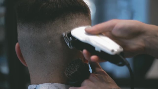 Close-up view on male's hairstyling in a barber shop with professional trimmer. Man's haircutting at hair salon with electric clipper. Grooming the hair.