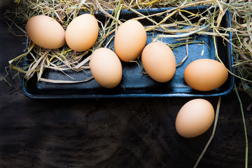 Many fresh eggs are placed on a straw in a foam tray placed on an old wooden floor. On the farmer's farm that is stored for family consumption and for sale
