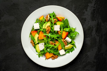Avocado salad with baby spinach and pomegranate on a white plate on the background of slate, stone or concrete.