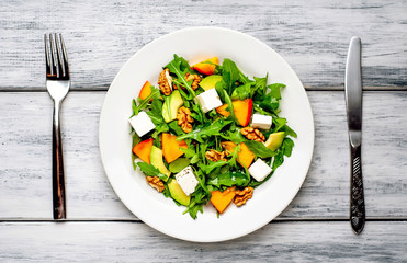 Arugula salad, persimmon, walnuts, avocados, feta cheese on a white plate on a wooden table