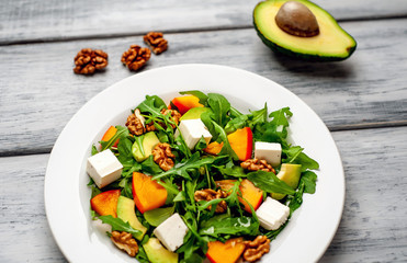 Arugula salad, persimmon, walnuts, avocados, feta cheese on a white plate on a wooden table