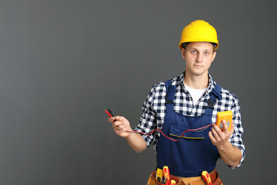 Electrician with multimeter wearing uniform on gray background. Space for text