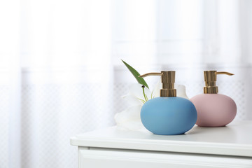 Stylish soap dispensers and lily on table against blurred background. Space for text