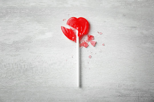 Broken heart shaped lollipop on gray background, top view. Relationship problems