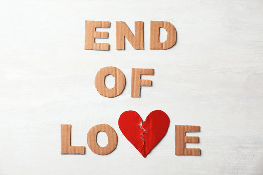 Phrase "End of love" with torn cardboard heart and letters on light background, top view. Relationship problems