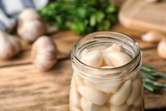 Preserved garlic in glass jar on table, closeup. Space for text