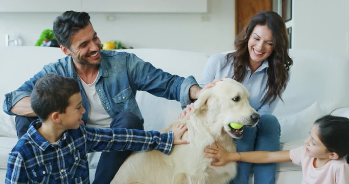 Portrait of happy family cuddling their dog having fun together in living room in slow motion. Shot with RED camera in 8K. Concept of happy family, parenthood, love for animals