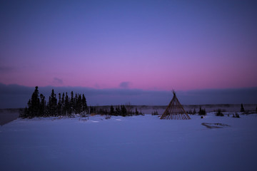 Cree teepee frame at dusk by a misty river in the remote northern boreal forest of Quebec