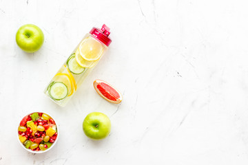 Fototapeta na wymiar Diet rich in fruits. Slimming diet. Fruit salad near fruit lemon and cucumber water on white stone background top view copy space