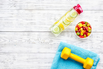 Healthy lifestyle, healthy habits. Detox water, fruit salad, sport equipment dumbbells on white wooden background top view copy space