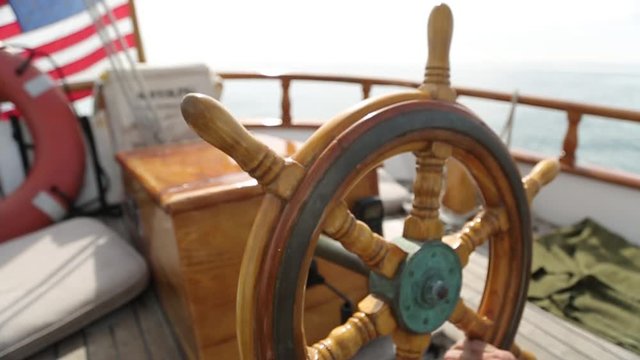 Closeup of a wheel and deck of a wooden antique sailing yacht rotating  steering wheel of Sail boat navigating in the ocean sunny day showing the wooden parts and accessories compass and detail aftern