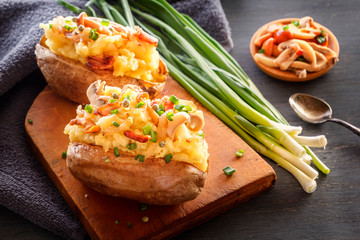Baked potatoes with bacon, mushrooms and green onions in a rustic style on a wooden board. Close-up