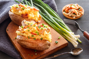 Baked potatoes with bacon, mushrooms and green onions in a rustic style on a wooden board. Close-up