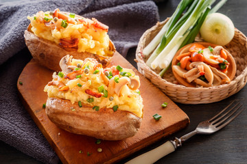 Baked potatoes with bacon, mushrooms and green onions in a rustic style on a wooden board. Close-up