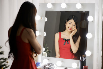 Attractive smiling Vietnamese young woman looking at her reflection in vanity mirror