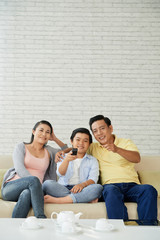 Smiling Asian family of three sitting on sofa and enjoying good movie on tv