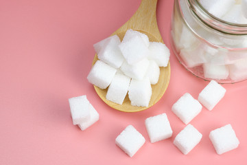 Cube granulated sugar in a glass jar and  on wooden spoon for adding sweetness. some parts was poured on a pink background. - image