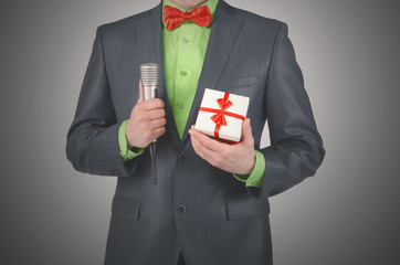 Gift box with a red bow and a radio microphone in a presenter hands on a gray background.