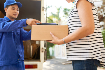 Woman taking parcel and tablet computer to sign for delivery