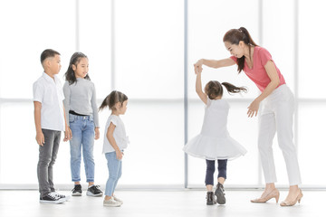 Fototapeta premium Asian woman in pink shirt dance with little Asian girl, Asian boy and gilrs look at them, they stand in front of big white window.