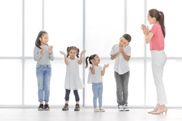 Asian woman in pink shirt teach Asian boy and girls to playing something , they stand in front of big white window.