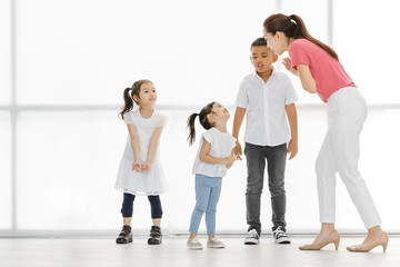 Fototapeta premium Asian woman in pink shirt teach Asian boy and girls to playing something , they stand in front of big white window.