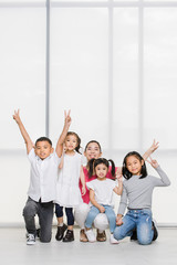 Fototapeta premium Smile Asian woman in pink shirt and Asian boy and girls squat on floor together, big white window behind them.