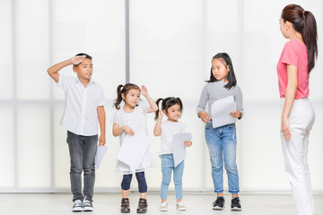 Asian woman in pink shirt and  Asian girls and boy  look at paper in her hands, they stand in front of big white window.