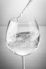 Water pouring into clear wine glass on white background 