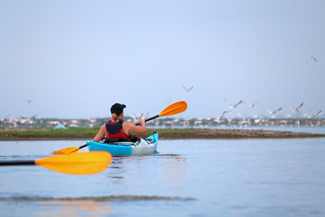 Man in kayak against the background of pelicans sitting on a sandy spit. Delta of Danube River near...