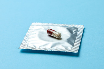 Birth control pills and condom in package on blue background. The concept of choosing method of contraception, birth control pills or condom