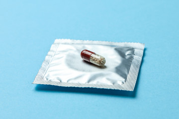 Birth control pills and condom in package on blue background. The concept of choosing method of contraception, birth control pills or condom