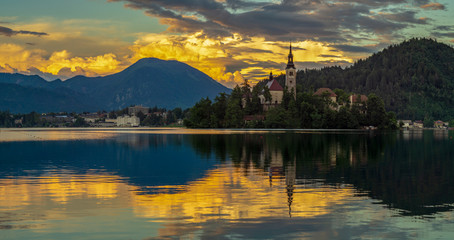 Naklejka na ściany i meble Beautiful, majestic storm clouds lit by the setting sun at Lake Bled in Slovenia