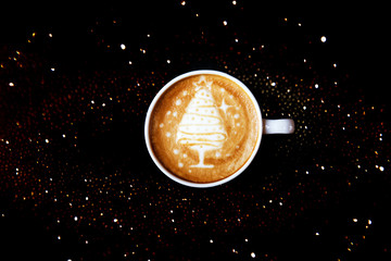 Tasty cappuccino with Christmas tree latte art with some blurred lights.