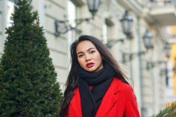 Portrait of a young beautiful fashionable woman in a red coat . Model posing on a city street