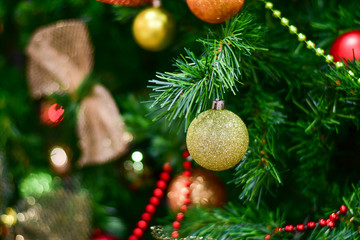 Christmas background: yellow and red balls on the green branches of the Christmas tree, golden bow, festive decor, festive atmosphere, gifts under the Christmas tree. new year 2019, selective focus 